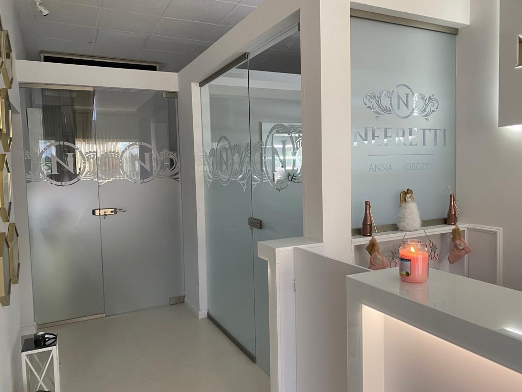 Szklane drzwi i ścianki działowe z dekoracyjnym motywem firmy Neffretti w Szczecinie, widoczne z perspektywy recepcji z zapaloną świecą i ozdobami.