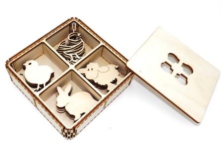 Drewniana szkatułka z przegródkami, zawierająca wycięte laserowo kształty: kurczaka, baranka, zajączka i ptasiego gniazda; obok leży drewniana pokrywka z wyciętymi czterema otworami w kształcie jajek.