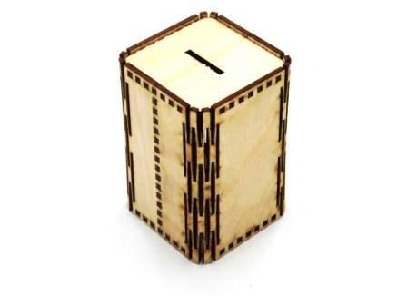Niezwykła, drewniana skarbonka w kształcie sześcianu, wykonana z jasnego drewna z ciemnobrązowymi krawędziami, na białym tle. Widoczna szczelina na górze.