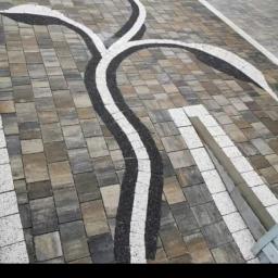 Profesjonaliści - Wzór z ciemnego żwiru wkomponowany w szaro-beżową kostkę brukową, tworzący faliste ścieżki na podjeździe.