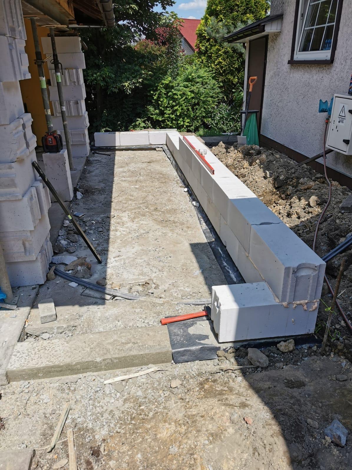 Budowa fundamentu z bloczków betonowych na zewnątrz budynku, widoczna poziomica i narzędzia budowlane