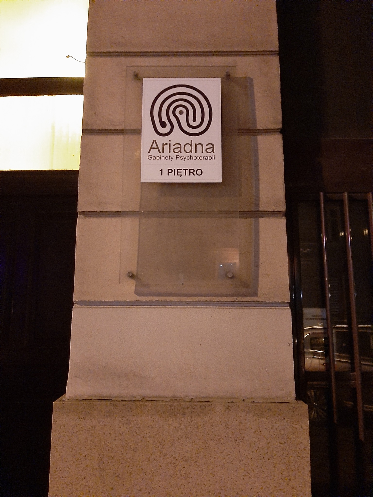 Szyld gabinetu psychoterapii Ariadna na pierwszym piętrze, z logo w formie labiryntu, umieszczony na kamiennej kolumnie budynku.