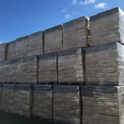 Sztaple palet z drewnem opałowym w przezroczystej folii na tle błękitnego nieba.