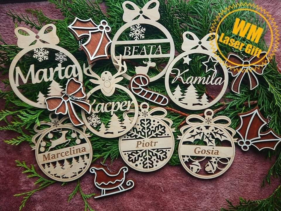 Ozdoby choinkowe z wygrawerowanymi imionami Marta, Beata, Kamila, Kacper, Marcelina, Piotr i Gosia, wykonane z jasnego drewna, ułożone na gałązkach igliwia.