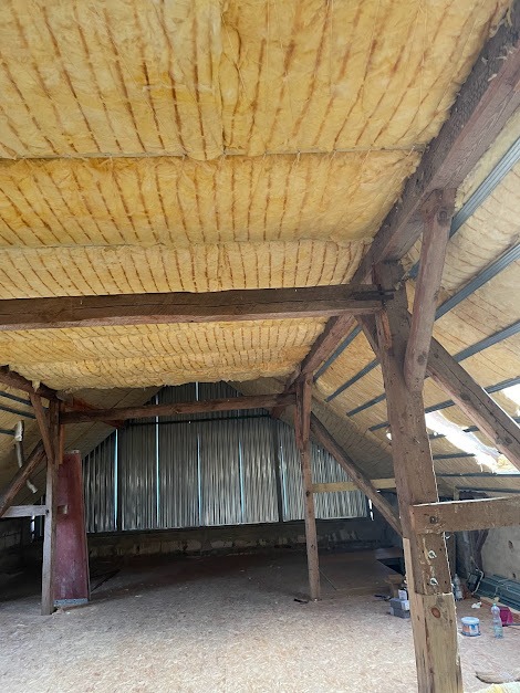 Poddasze z widoczną izolacją termiczną z wełny mineralnej, drewniana konstrukcja więźby dachowej, blaszane poszycie dachu w tle.