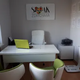 Jasne biuro z zielonym akcentem w postaci krzeseł i laptopa, w tle logo 'Smak Zdrowia' i certyfikaty, w rogu waga analityczna.