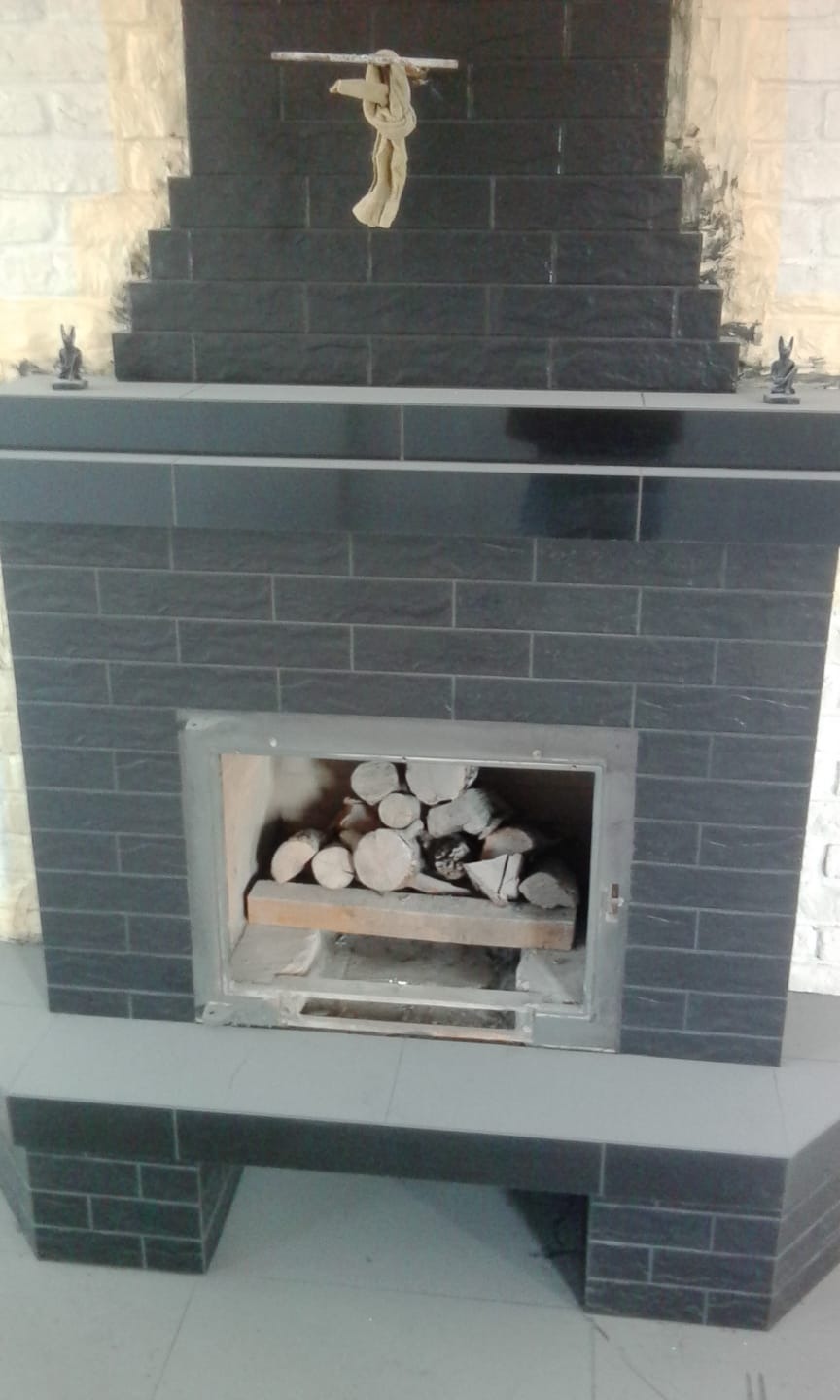 Wykończony kominek z czarnej cegły z drewnem w środku, ozdobiony figurkami i szmatką na drążku.