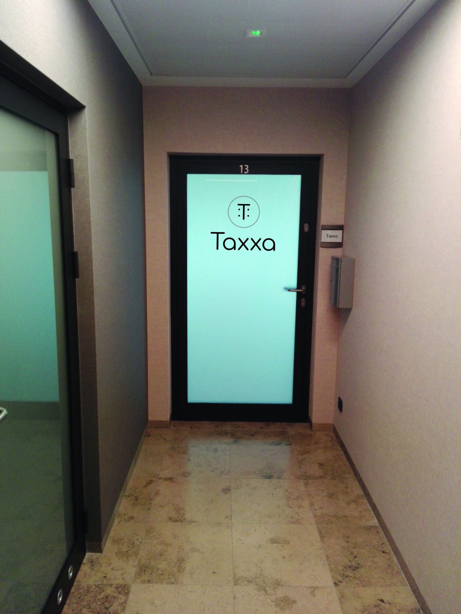 Korytarz biurowy z drzwiami do biura rachunkowego Taxxa, numer 13 nad drzwiami, tabliczka z nazwą firmy na ścianie, marmurowa podłoga.