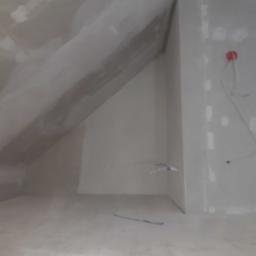 REM-BUD Sp. z o.o. - Poddasze z ukośnym sufitem w trakcie prac wykończeniowych, ściany pokryte gładzią gipsową z widocznymi łatami, instalacja elektryczna w puszce.