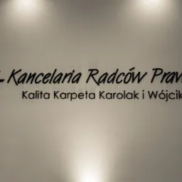 Tablica z czarnym, przestrzennym napisem: Kancelaria Radców Prawnych Kalita Karpeta Karolak i Wójcik s.c., umieszczona na jasnej ścianie pod delikatnym oświetleniem punktowym.
