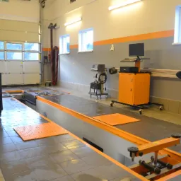 Stanowisko do geometrii kół w warsztacie samochodowym z podnośnikiem zagłębionym w posadzce, szafka narzędziowa na kółkach oraz sprzęt diagnostyczny.