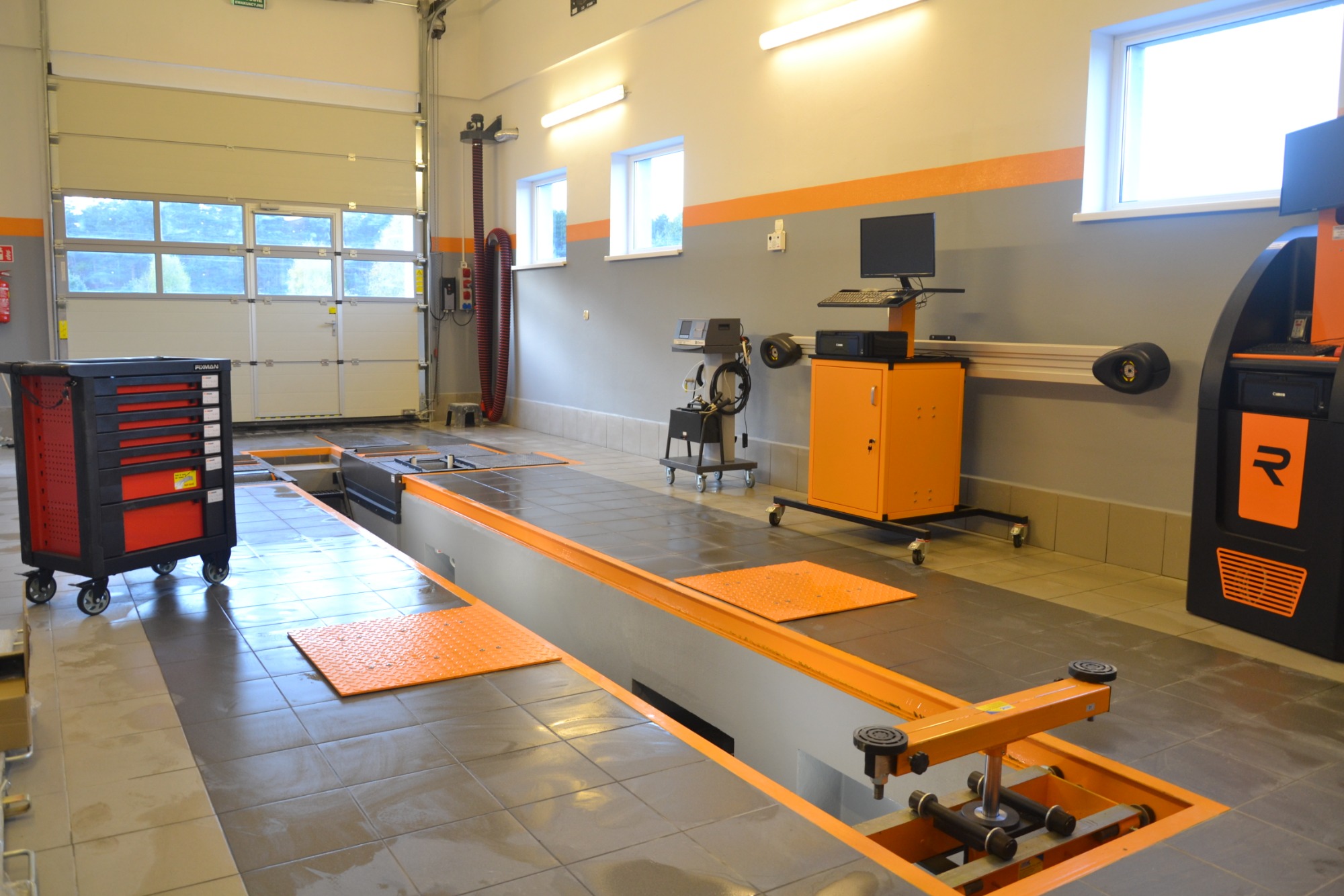 Stanowisko do geometrii kół w warsztacie samochodowym z podnośnikiem zagłębionym w posadzce, szafka narzędziowa na kółkach oraz sprzęt diagnostyczny.