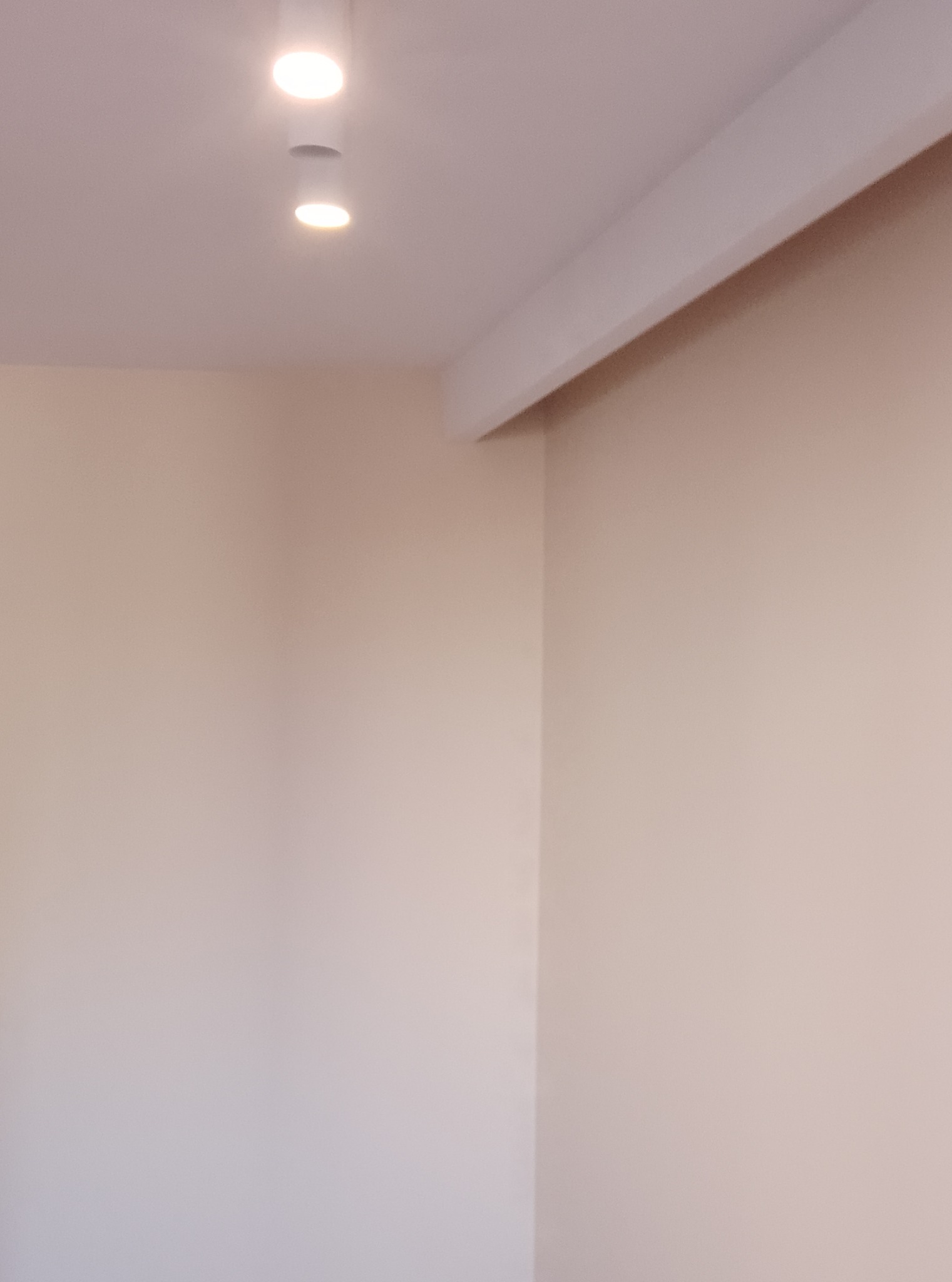 Wnętrze pokoju po remoncie, ściany pomalowane na jasny beż, widoczne oświetlenie sufitowe punktowe i biały element dekoracyjny pod sufitem.