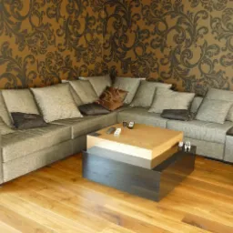 Szara narożna sofa z poduszkami w salonie z drewnianą podłogą i stolikiem kawowym na dwóch poziomach, z pilotami na blacie, na tle ściany z wzorzystą tapetą.