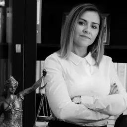 Portret kobiety w białej koszuli z założonymi rękami na tle biblioteczki i figury Temidy, Krosno Odrzańskie, czarno-białe zdjęcie.