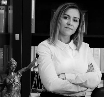 Portret kobiety w białej koszuli z założonymi rękami na tle biblioteczki i figury Temidy, Krosno Odrzańskie, czarno-białe zdjęcie.