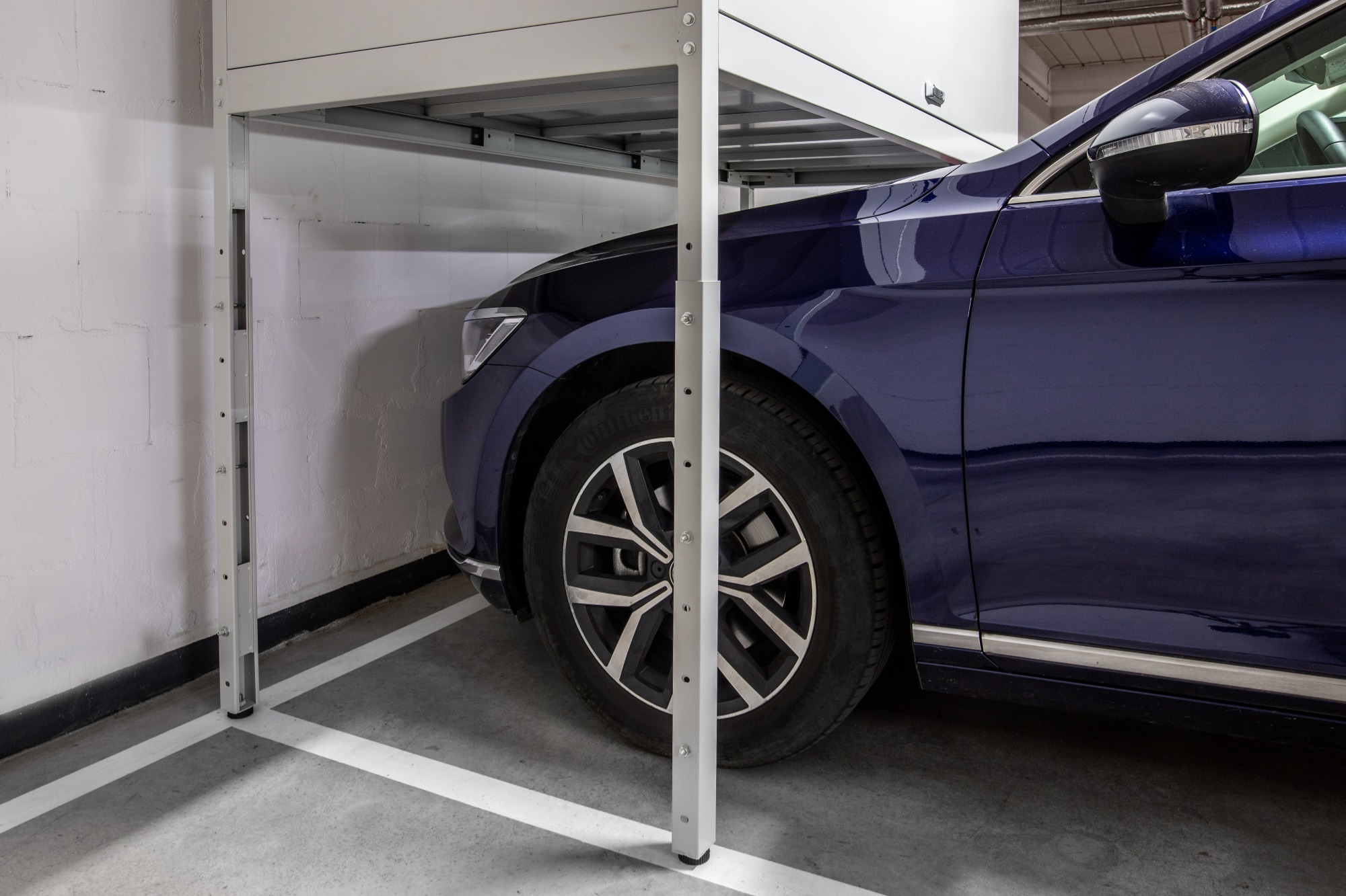 Szafa garażowa z metalową konstrukcją nad zaparkowanym, granatowym samochodem osobowym na betonowej posadzce garażu.