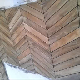 Ułożone w jodełkę drewnopodobne kafelki z ciemnymi fugami na ścianie, widoczne ślady świeżego montażu przy suficie.