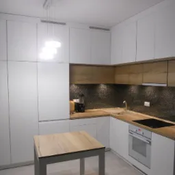 Nowoczesna kuchnia w bieli i drewnie z geometrycznym wzorem na ścianie nad blatem, oświetlona wiszącą lampą z trzema kwadratowymi kloszami.