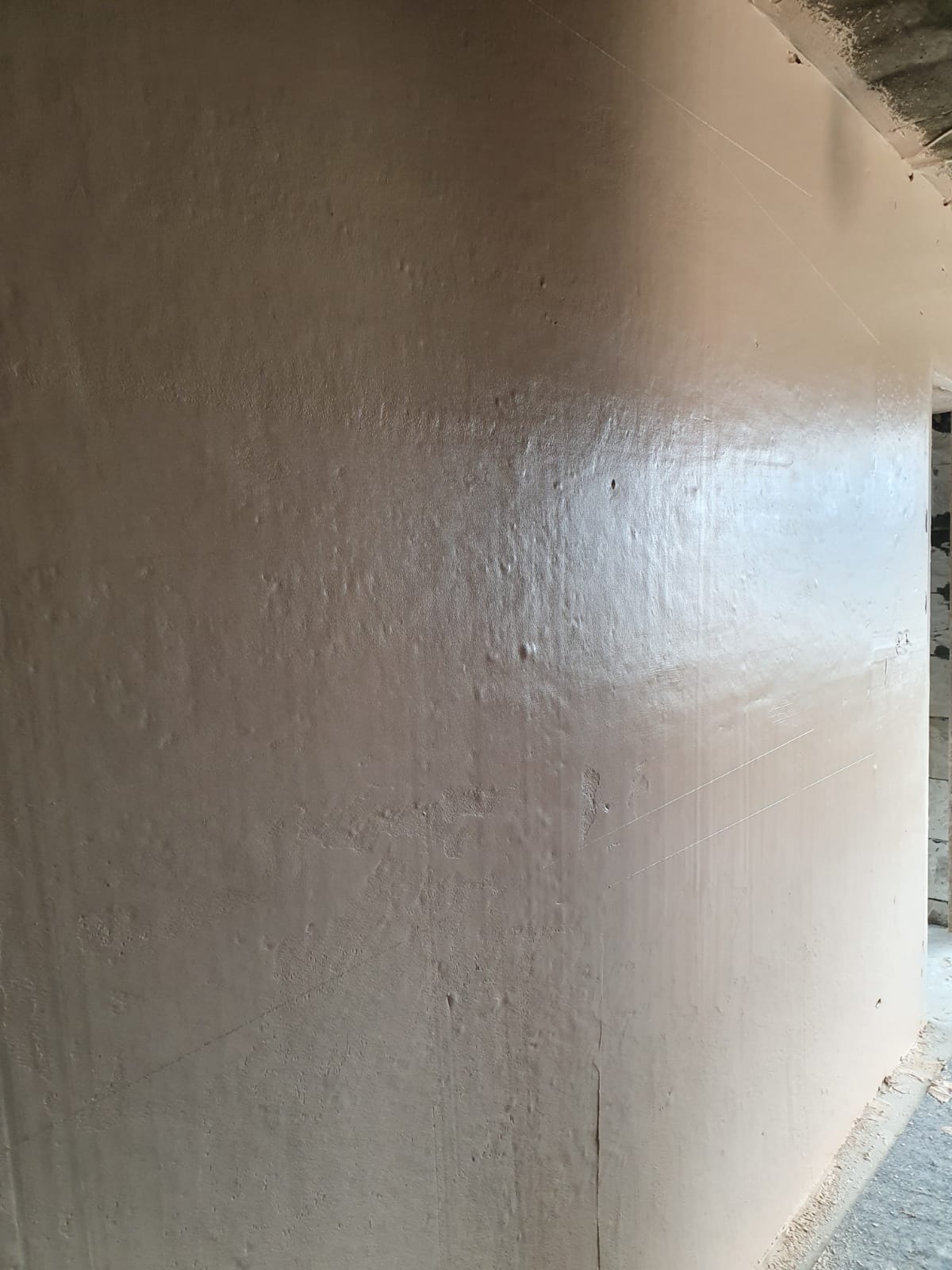 Świeżo nałożona warstwa tynku na ścianie wewnętrznej, widoczne drobne nierówności i delikatne ślady narzędzi, oświetlenie boczne podkreśla fakturę powierzchni.