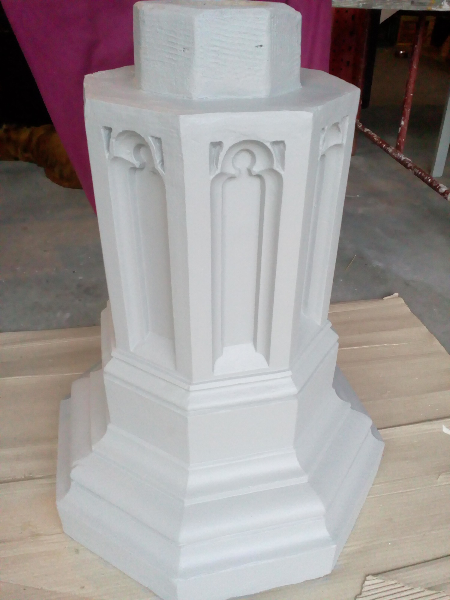 Świeżo pomalowany na biało fragment kolumny dekoracyjnej z motywem gotyckim, widoczne detale architektoniczne i niedoskonałości malowania, ustawiony na tekturze.