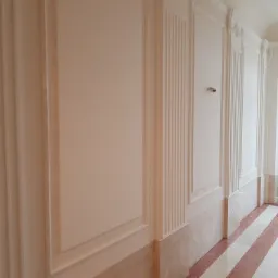 Korytarz po remoncie z dekoracyjnymi panelami ściennymi w odcieniach bieli i beżu, z fragmentem surowej cegły po lewej stronie i marmurową podłogą w paski.