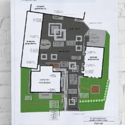 Plan zagospodarowania przestrzeni przydomowej z oznaczeniami materiałów, uwzględniający budynek mieszkalny i gospodarczy, z zaznaczeniem nawierzchni z kostki, obrzeży i zieleni.