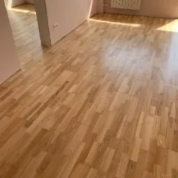 Świeżo ułożona, jasna podłoga parkietowa w jodełkę klasyczną, w pokoju z różowymi ścianami i grzejnikiem pod oknem, widok z góry.