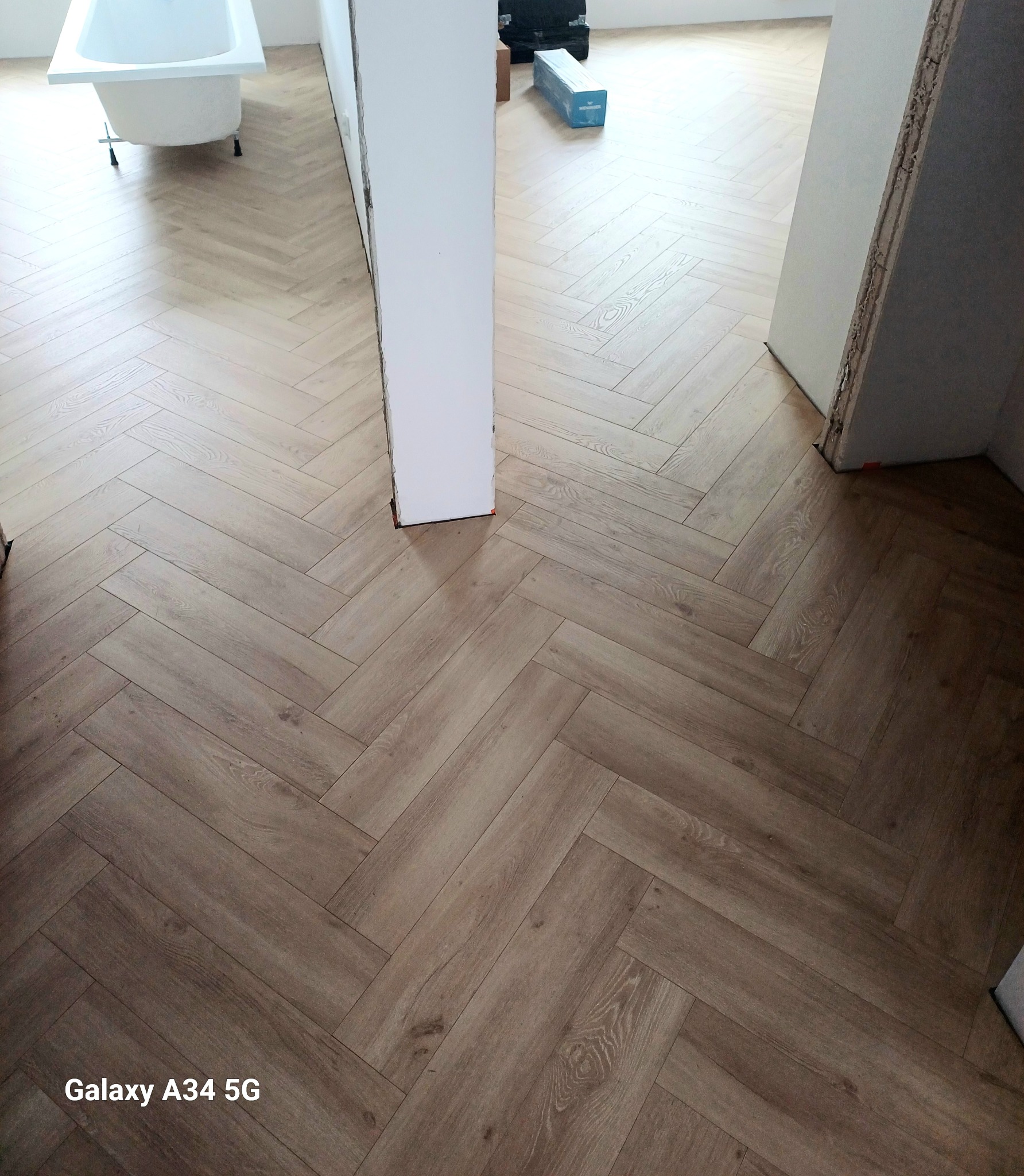 Ułożona jasna podłoga w jodełkę w trakcie remontu łazienki, widoczna biała wanna na nóżkach i niedokończone obramowanie drzwi.