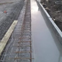 Przygotowany szalunek z ułożonym zbrojeniem i świeżo wylanym betonem na fundamencie budynku w trakcie budowy.