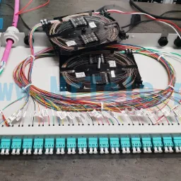 Panel światłowodowy z kolorowymi kablami uporządkowanymi wewnątrz obudowy, zakończonymi złączami oznaczonymi etykietami, z dwoma organizerami kabli na górze.