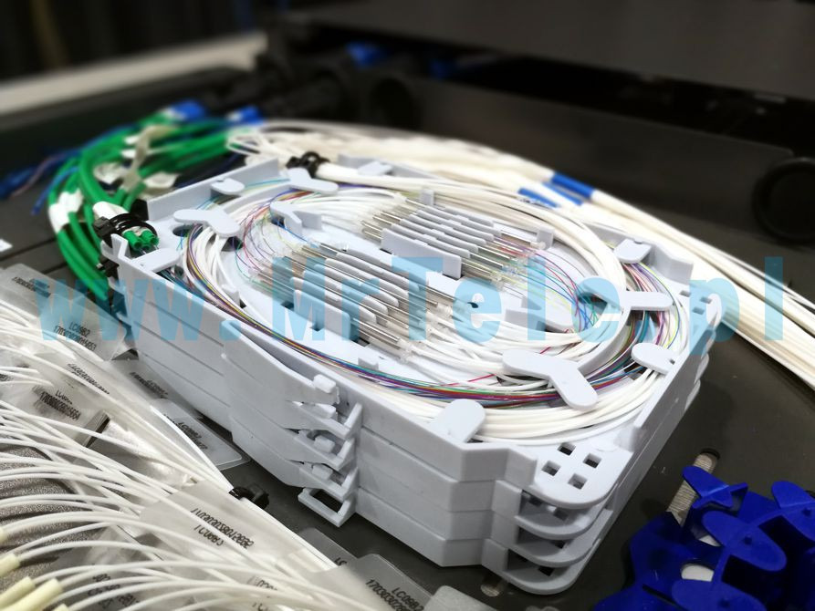 Rozdzielnica światłowodowa z widocznymi kablami światłowodowymi w kolorach białym, zielonym i niebieskim, uporządkowanymi wewnątrz kasety światłowodowej z adapterami.