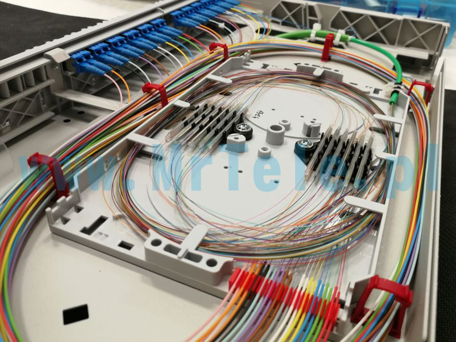 Otwarta skrzynka światłowodowa z uporządkowanymi, kolorowymi kablami, złączami i elementami montażowymi, widoczne uchwyty kablowe.