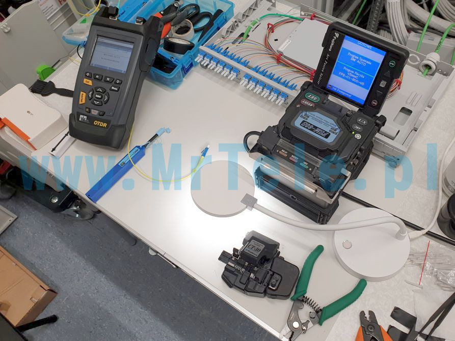 Sprzęt do spawania światłowodów (spawarka Fujikura), reflektometr OTDR oraz narzędzia na stole roboczym podczas instalacji sieci światłowodowej w Gdańsku.