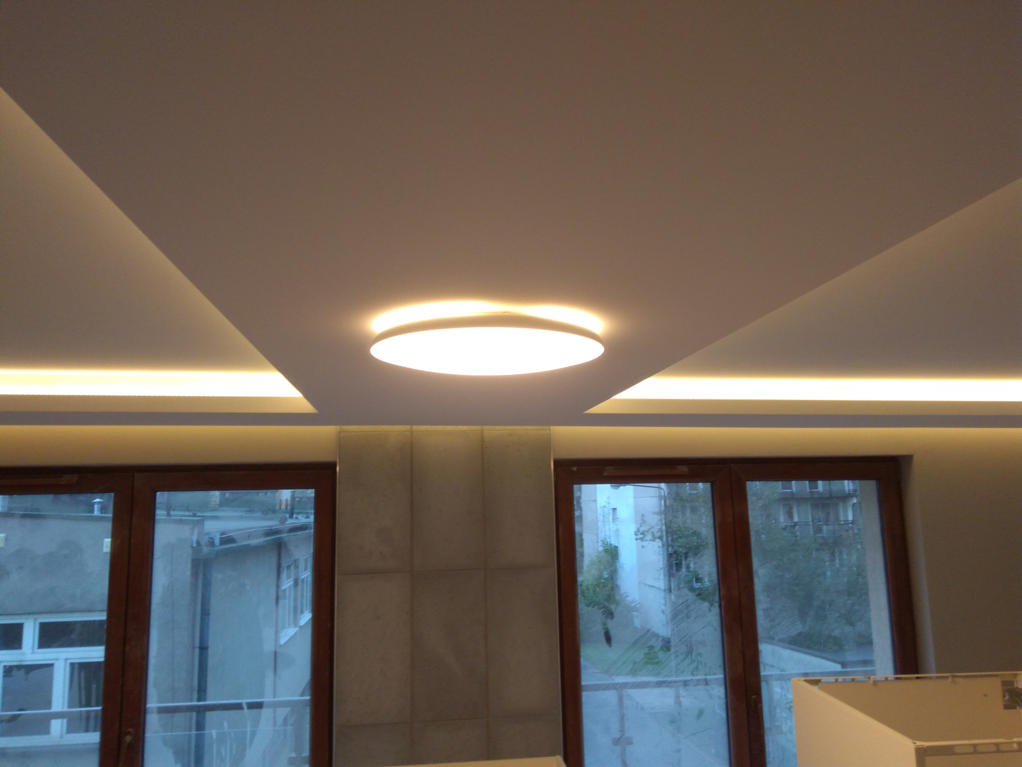 Nowoczesny sufit z oświetleniem LED, okrągła lampa sufitowa, widok na budynki mieszkalne przez okna