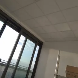 Montaż sufitu podwieszanego kasetonowego w pomieszczeniu z dużym oknem przesuwnym, widoczny fragment rusztowania i karton z płytami.