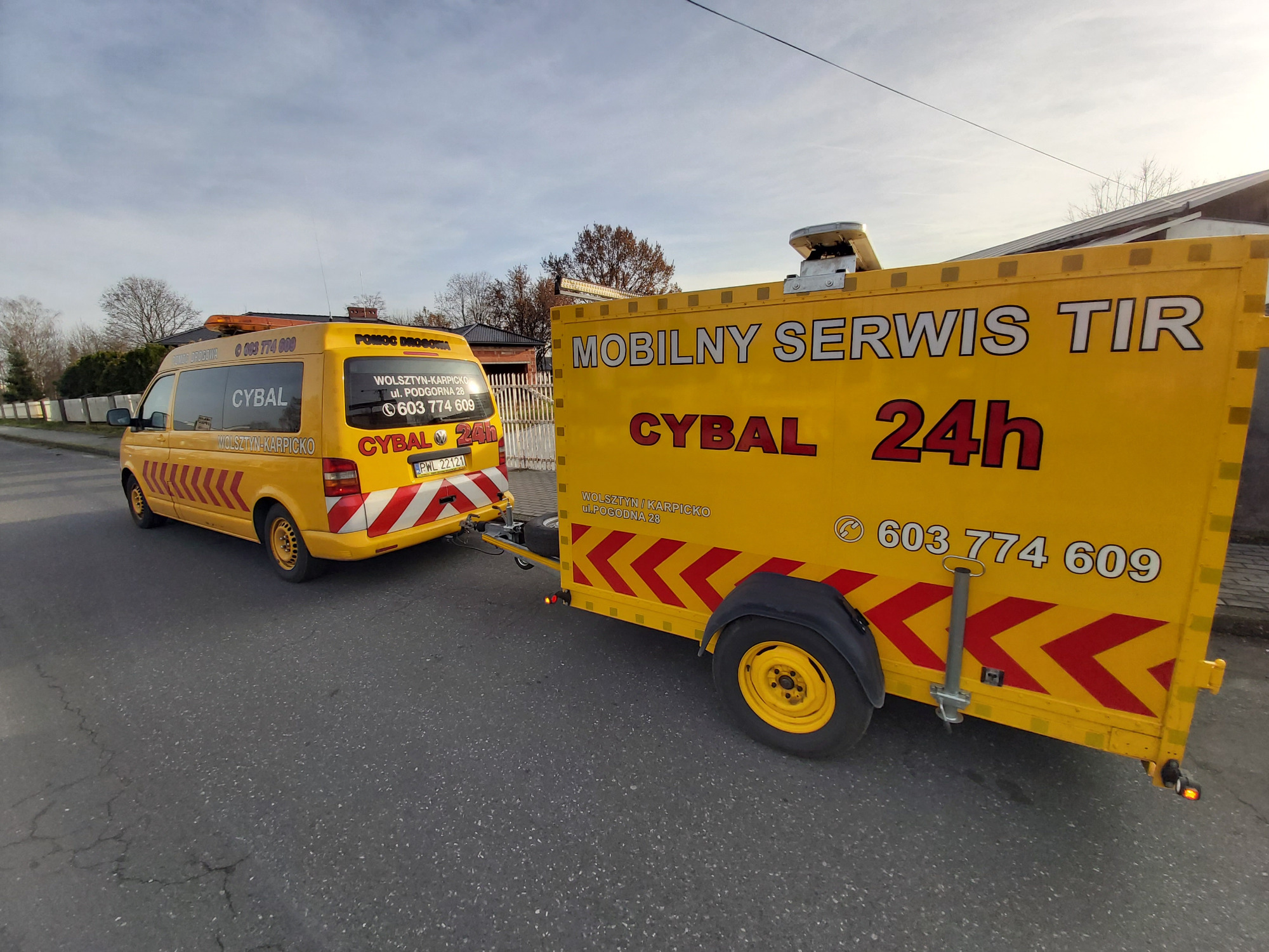 Żółty bus pomocy drogowej z przyczepą serwisową TIR na ulicy w dzień, widoczne numery telefonów i logo firmy.