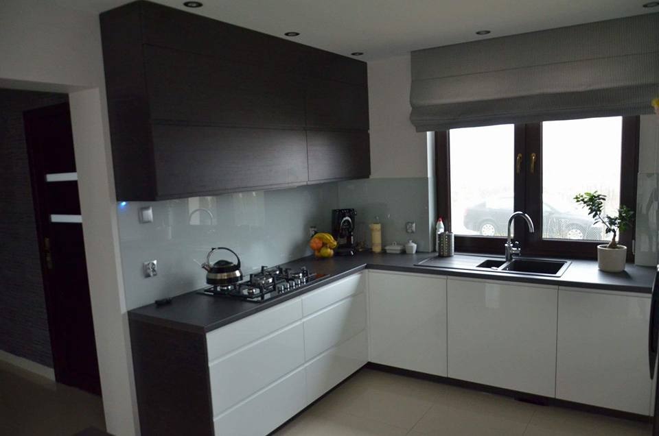 Nowoczesna kuchnia z białymi szafkami dolnymi i ciemnobrązowymi górnymi, szary blat, okno z roletą rzymską, czajnik na płycie gazowej.