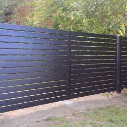 Przemysław Markiewicz - Nowoczesna, pozioma, czarna brama wjazdowa, widoczna od strony podwórza, z fragmentem białego samochodu dostawczego po prawej i ceglanym murem w tle.