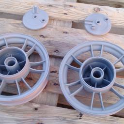 Sandblast - Dwa szare, metalowe koła i dwa okrągłe elementy, prawdopodobnie po procesie nałożenia powłoki, leżące na drewnianej palecie. Widoczne delikatne refleksy światła na powierzchni.