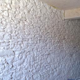 Sandblast - Wnętrze budynku z nierówną, białą ścianą imitującą kamień, widoczne fragmenty sufitu i drzwi w tle.