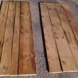 Sandblast - Dwie drewniane konstrukcje z desek leżące na szarym podłożu, jedna po lewej stronie ciemniejsza, po prawej jaśniejsza, widoczne słoje drewna i ślady po obróbce.