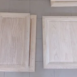 Drewniane fronty szafek po piaskowaniu, ukazujące strukturę drewna i przygotowane do dalszej obróbki, leżące na podłodze z płytek.