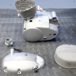 Sandblast - Elementy silnika motocyklowego Predom-Dezamet po renowacji, pokryte srebrzystą farbą, leżące na gumowej macie. Widoczny cylinder, karter i dwie pokrywy.