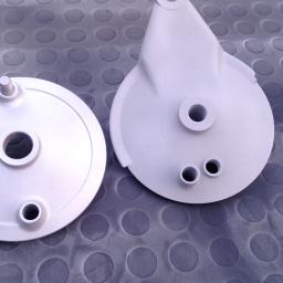 Sandblast - Dwie piasty hamulcowe motocyklowe, po obróbce, leżą na gumowej macie z wytłaczanymi kółkami. Piasty mają srebrzysto-szary matowy odcień.