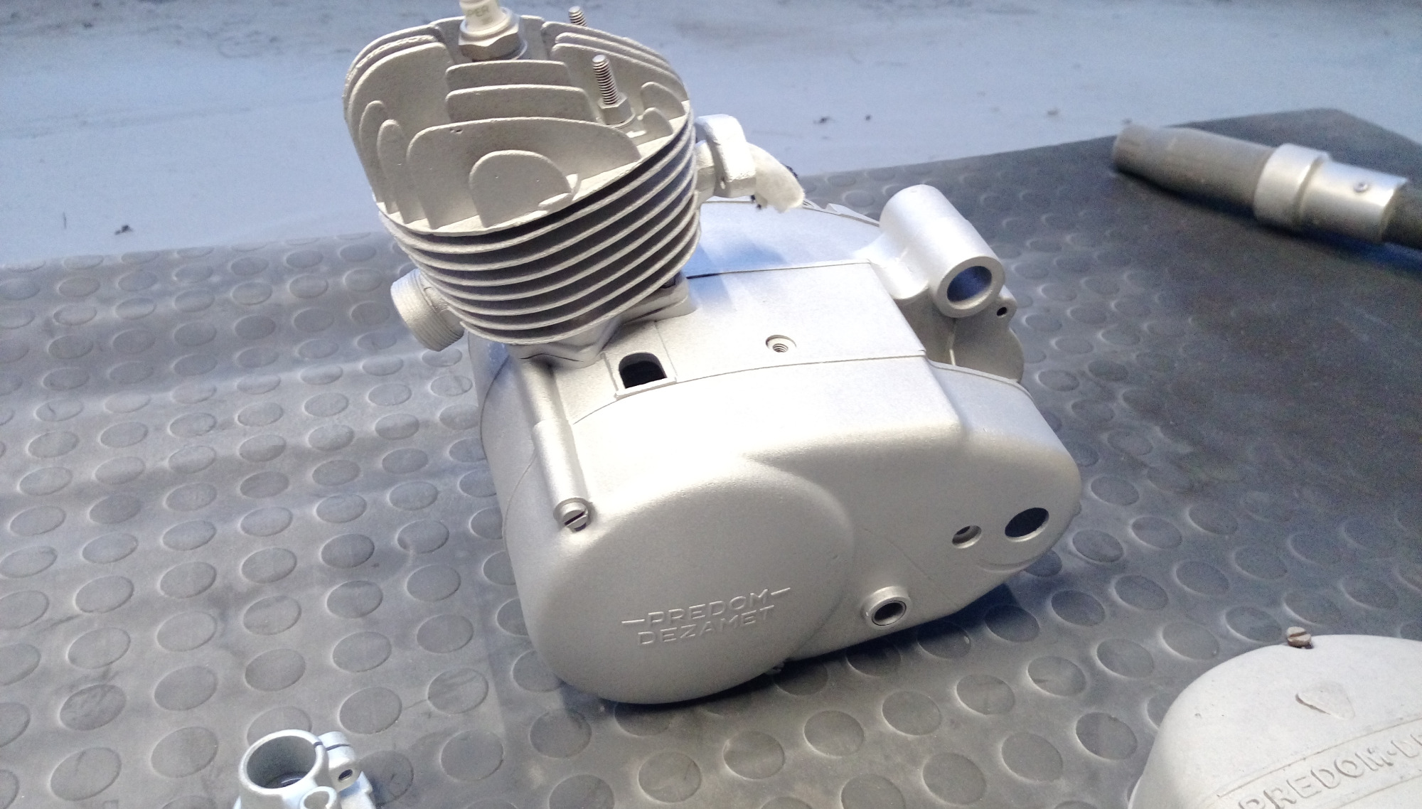 Elementy silnika motocyklowego po renowacji, pokryte srebrną farbą, widoczne napisy 'Predom-Dezamet'.