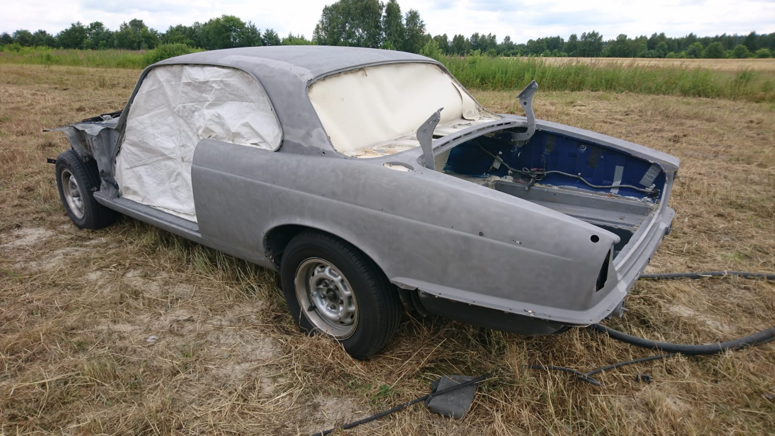 Przygotowanie do malowania klasycznego samochodu w Winiarach Dolnych: karoseria po piaskowaniu, zabezpieczona folią, z otwartą maską, widoczne ślady po procesie.