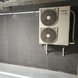 Zewnętrzna jednostka klimatyzacji Toshiba Mini SMMS zamontowana na szarej ścianie z betonowych bloków w garażu podziemnym, widoczne rury i wsporniki montażowe.