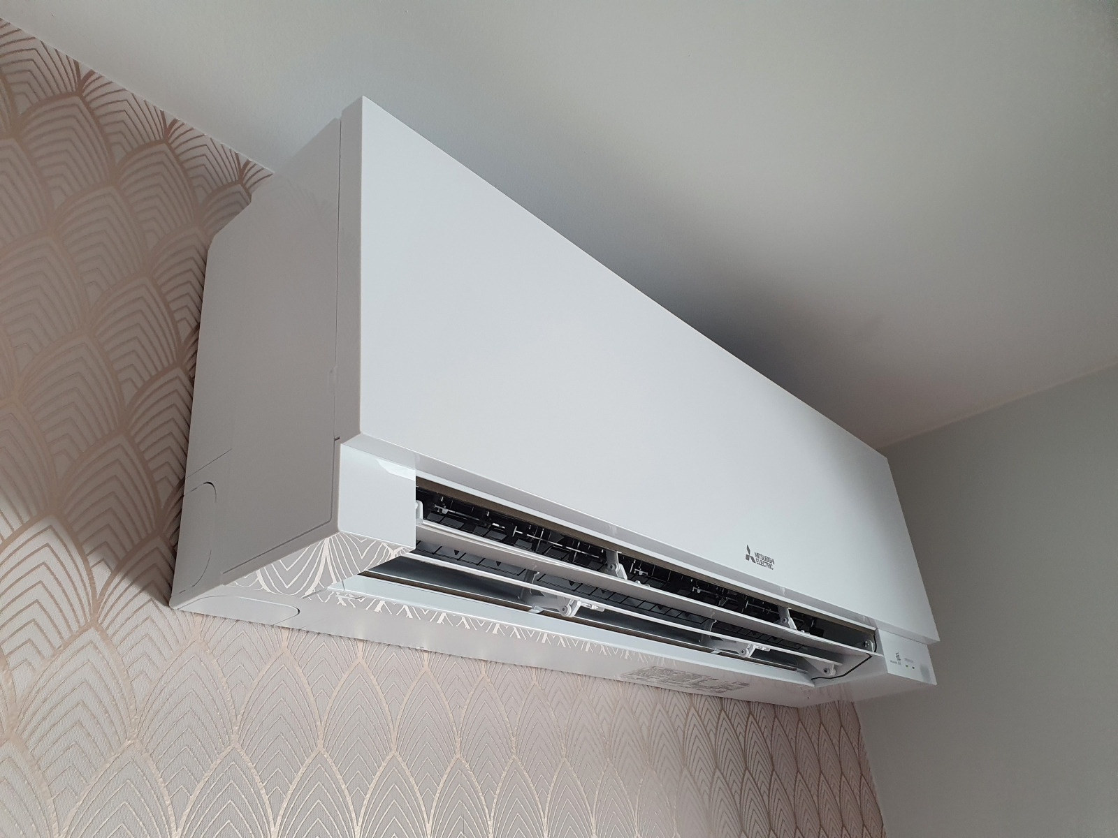 Biała jednostka wewnętrzna klimatyzacji Mitsubishi Electric MSZ-EF Premium zamontowana na ścianie z wzorzystą tapetą, widok z dołu.