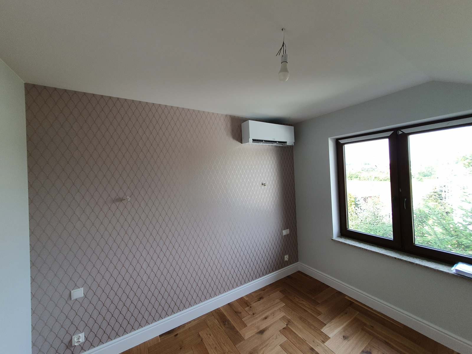 Biała jednostka klimatyzacyjna Mitsubishi Electric MSZ-EF Premium zamontowana na wzorzystej ścianie w pokoju z parkietem i oknem.